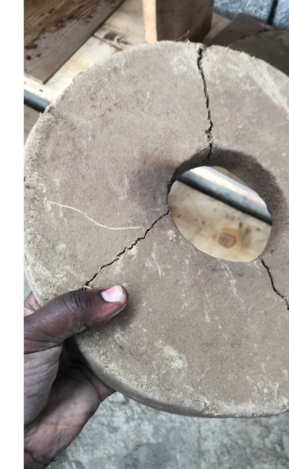 Close-up of a cracked concrete or clay disc, split cleanly down the middle, held in a producer's hand