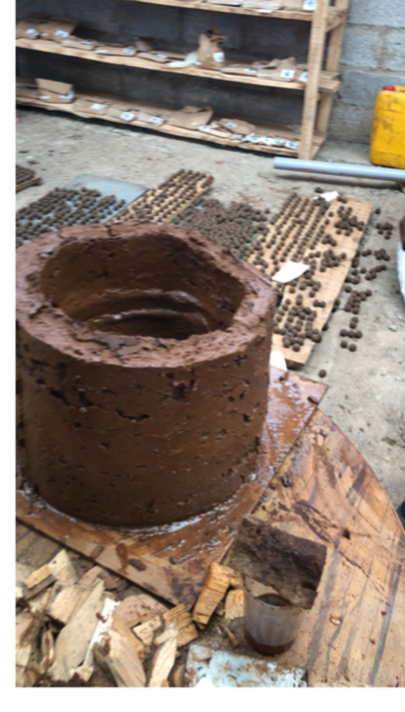 Hollow clay stove body drying on a wooden board in the production shed