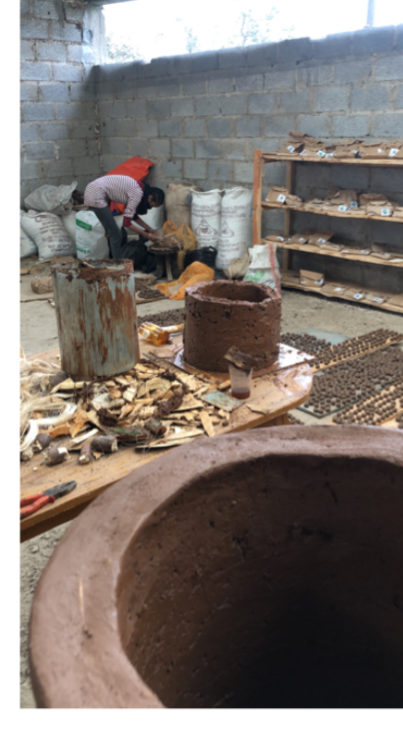 Wide clay stove body next to wood chips in the production shed