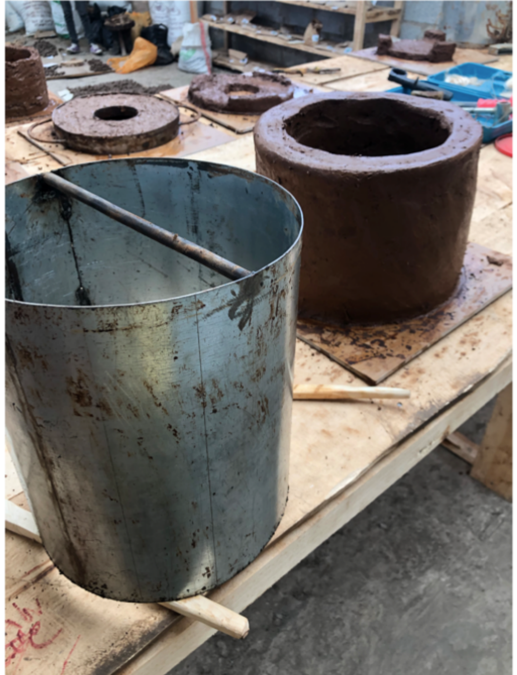 Improvised metal can mold next to a clay stove body on a wooden workbench